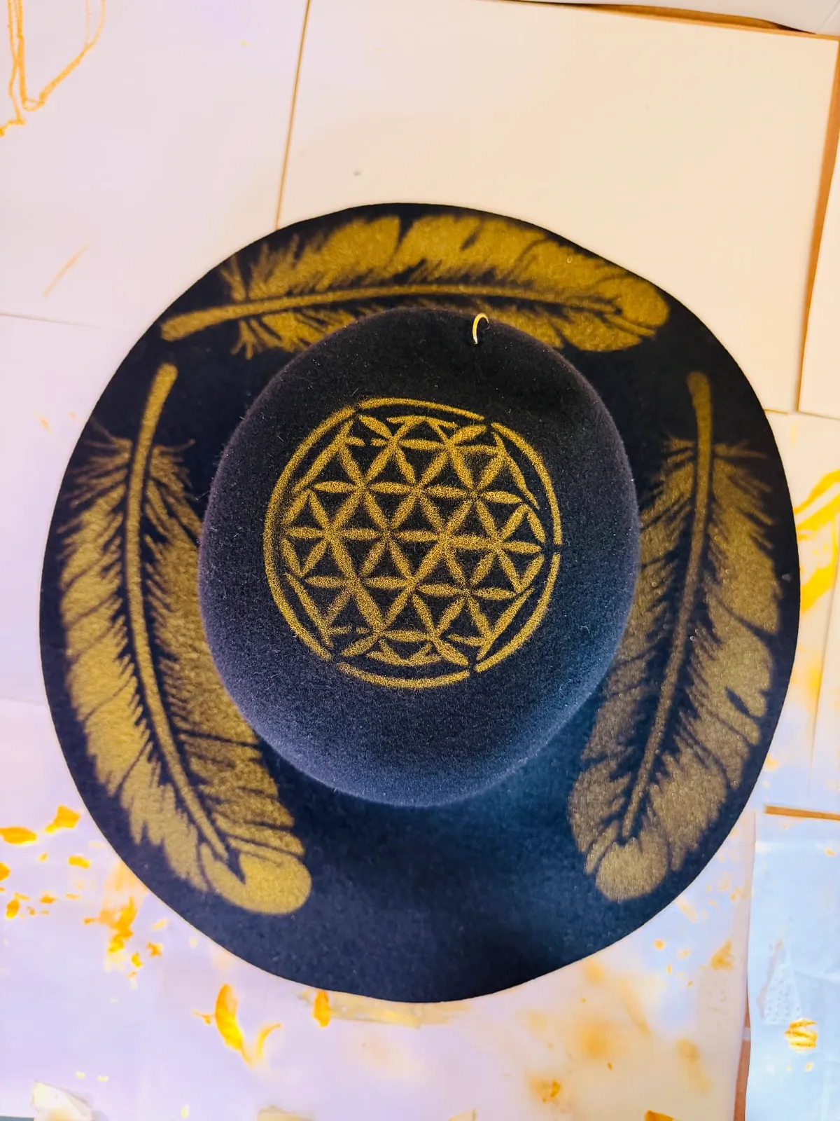 Completed painted design: gold feathers across the brim and a flower of life on the crown