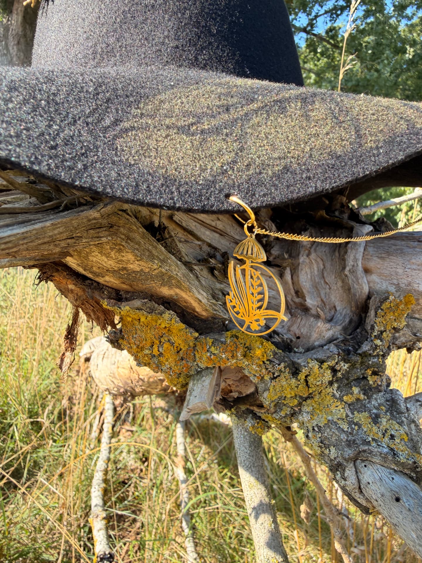 Schwarzer handgefertigter Hut mit goldenem Schmuckanhänger auf naturbelassenem Holz